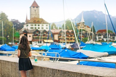a young girl strolls through the beautiful spa town of spiez, switzerland and looks at boats and yachts on the lake