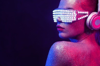 beautyful girl with glitter and sparkles on her face and body. portrait of sexy tdj with headphones and neon sunglasses