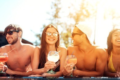 company of joyful friends drinks cocktail drinks in pool at summertime. swimming pool party. multiethnic company of friends in swimming pool.