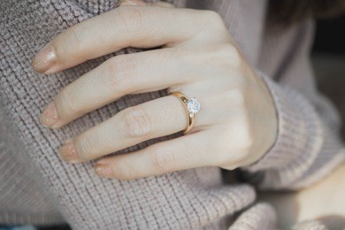 close up of an elegant engagement diamond ring on woman finger with dark pink sweater winter clothe. love and wedding concept.soft and selective focus.