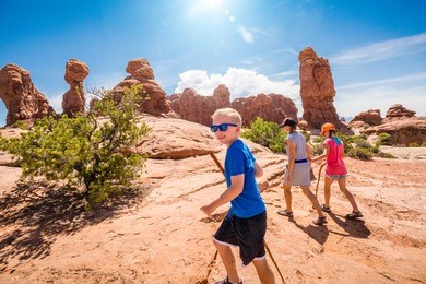 happy family hiking together in the beautiful rock formations of arches national park. walking along a scenic trail with large rock unique formations in the background