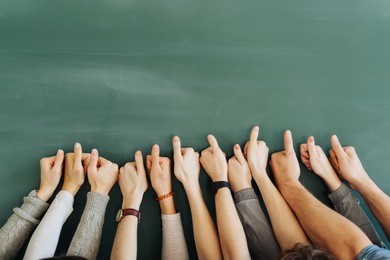 a team of students hands with thumbs up on a classroom blackboard.
