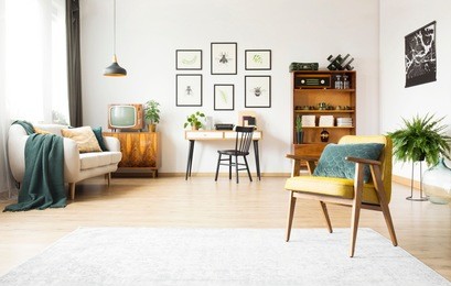 spacious living room interior with study space against white wall and green pillow on old armchair 