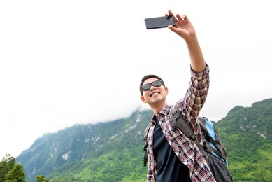 independent asian tourist man taking selfie with natural green mountain scenery during summer holidays in chiangmai thailand