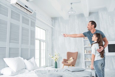 air conditioning. positive delighted joyful man standing together with his daughter and looking at the air conditioner while holding a remote control