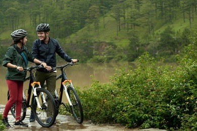 active asian couple looking at each other while walking with their bicycles on rainy day