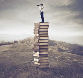 young businessman standing on a stack of books and using a telescope
