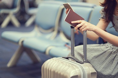 close up woman hand holding passport and playing smartphone on her suitcase at airport while waiting for boarding time ,traveler concept