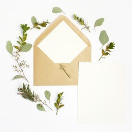 flat lay shot of letter and eco paper envelope on white background. wedding invitation cards or love letter with plant. valentine's day or other holiday concept. top view