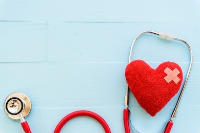 world health day, healthcare and medical concept. woman hand holding red heart with stethoscope, notepad, thermometer and yellow pill on pastel white and blue wooden table background texture.