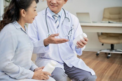 profile view of senior asian patient listening to her doctor with interest while he giving her instructions how to take pills correctly, interior of modern office on background