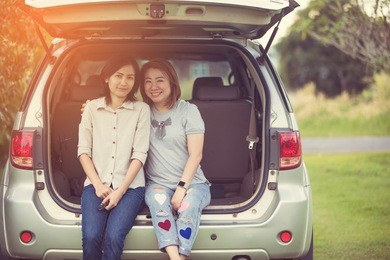 two glorious lesbians relax on the car in park.