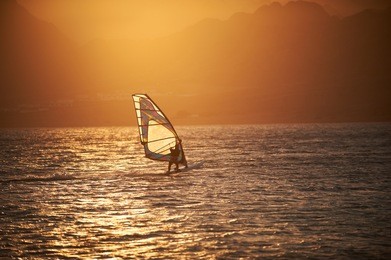 sportman windsurfer on the sea surface against mountains at sunset time