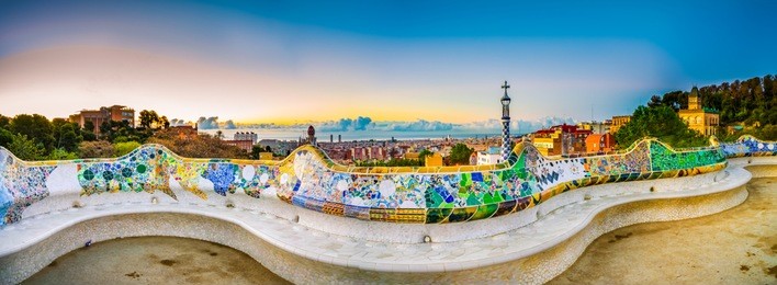 mosaic tile panorama and barcelona cityscape in famous park guell at summer sunset,spain