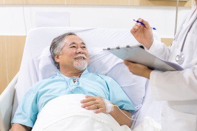old patient lying in hospital bed. doctor holding clipboard and taking to him.