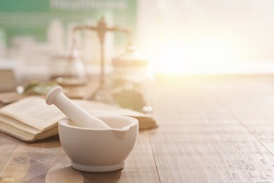 mortar and pestle with pharmaceutical preparations's book and herbs on a wooden pharmacist table, traditional medicine and pharmacy concept