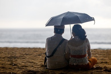 couple sitting by sea with an umbrella looking at storm on ocean horizon.