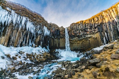 the dark falls (svartifoss) in skaftafell in national park iceland. it is a famous icelandic natural landmark. the water streaming hardly from black basalt cliff.it is in winter so the ice and snow.