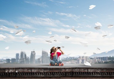 cute girl of school age on building roof looking in binoculars