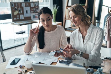 designing new clothes. beautiful young women working on sketches and swatches while sitting in the workshop 