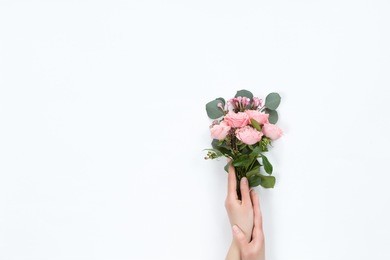 top view of floral composition of kraft cornet with beautiful pink rose flower bouquet in girls hand on white background, flat lay, copyspace