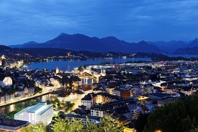 aerial panorama of beautiful lucerne city by lakeside with wooden chapel bridge ( kapellbrucke ) across reuss river & majestic rigi mountain in background at blue dusk before nightfall, switzerland