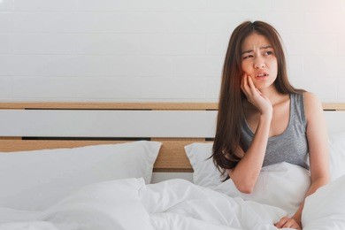 young asian woman feel toothache and discomfort on bed in white bedroom morning.concept of women's health care.