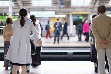 japanese people queuing, waiting for their commuter train in a busy railway station in tokyo on a bright spring day.
