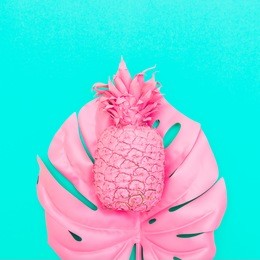 painted pink pineapple on tropical and palm leaf in vibrant bold color on turquoise background . concept art. minimal surrealism. flat lay 