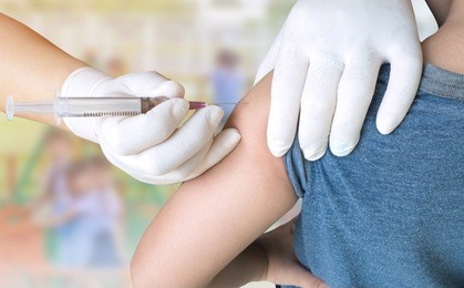 doctor woman giving a child injection in arm on burred student playing with toy on playground in the school.