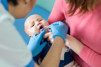 baby on mothers hand at hospital. nurse making infant oral vaccination against rotavirus infection. children health care and disease prevention.