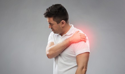 people, healthcare and problem concept - unhappy man suffering from pain in shoulder over gray background