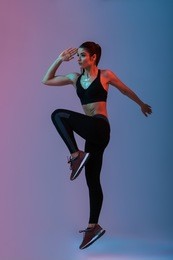 full length portrait of sportswoman 20s wearing black tracksuit practicing in gym and doing workout isolated over neon lights