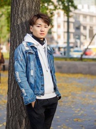 young chinese smiling man portrait stand with blur yellow trees background in sunset in autumn park. outdoor.
