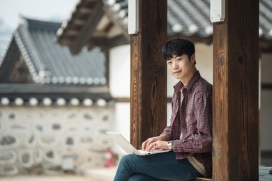 young man traveling in south korea. using a laptop sitting in a korean traditional house.