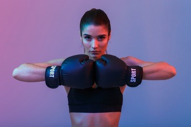 image of young sports woman in tracksuit and black putting hands together in boxing gloves isolated over purple background