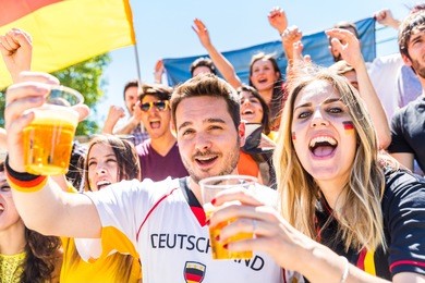 german supporters celebrating at stadium and drinking beer. group of fans watching a match and cheering team germany. sport and lifestyle concepts.