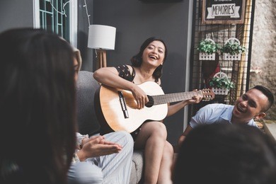 young happy friends having party, one playing guitar and the other singing together