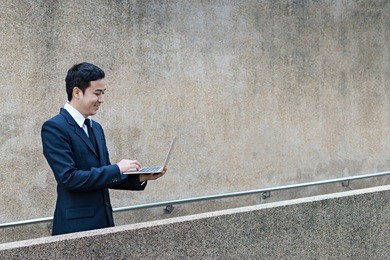 young asian businessman uses laptop computer outdoor to work online.