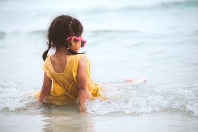 cute asian little child girl sitting and playing on beach in summer vacation in vintage color tone