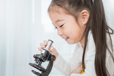 beautiful asian little girl looking at a microscope in a classroom. selective focus on microscope. education science project concept