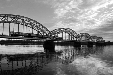 the train travels along the railway bridge across the daugava river with a beautiful reflection of the sky and clouds during the sunset in riga, latvia
