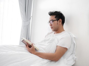 happy asian man reading a book on bed, man lifestyle on weekend concept.
