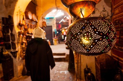 a woman walks past a lantern shop in a marrakech souk.