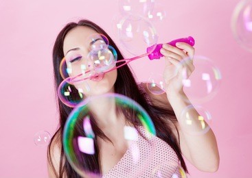 beautiful girl blowing soap bubbles in the studio on a pink background