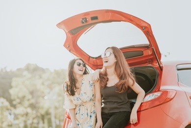 two happy asian girl best friends traveler laughing and smiling while sitting in red car trunk 