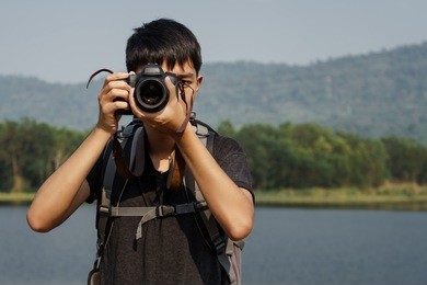 young asian backpack travelling. he use dslr camara to take a photo.
