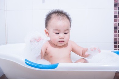 baby boy shower in bath with foam bubbles