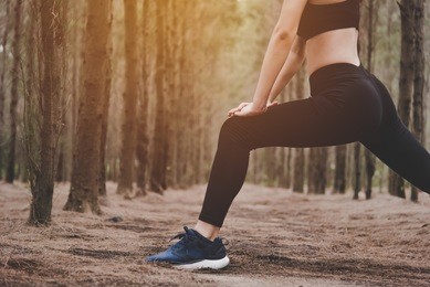 close up of lower body of woman doing yoga and stretching legs before running in forest at outdoors. sports and nature concept. lifestyle and activity concept. pine woods theme.