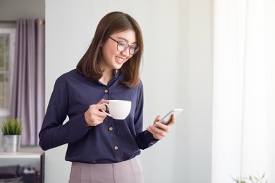 businesswoman using smart phone and holding coffee cup in living room